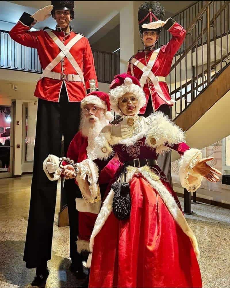 Professional Santa Claus with Mrs. Claus and two stilt nutcracker soldiers by a staircase.