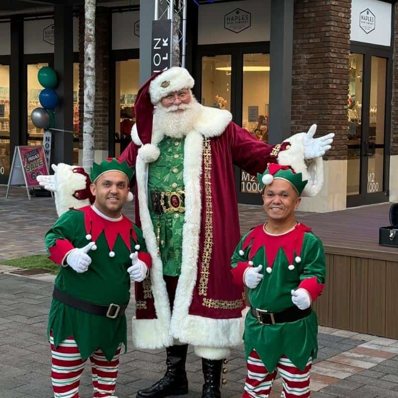 Santa Claus impersonator in Atlanta with two elves in green costumes giving thumbs up.